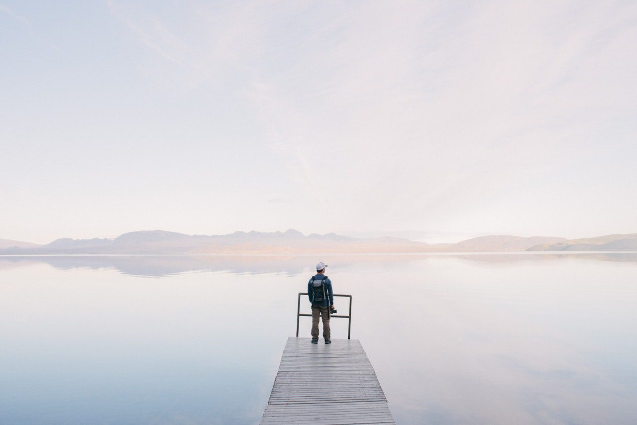 A lone man stand at the end of a dock looking at the low water levels of a lake