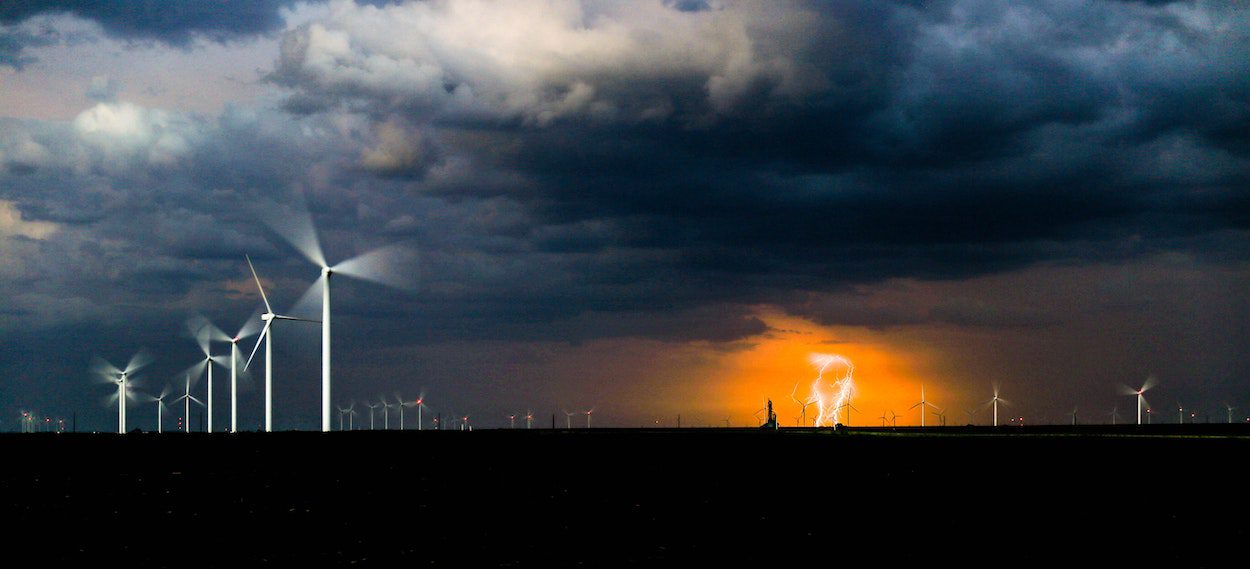 An image of offshore wind turbines with lightning in the distance