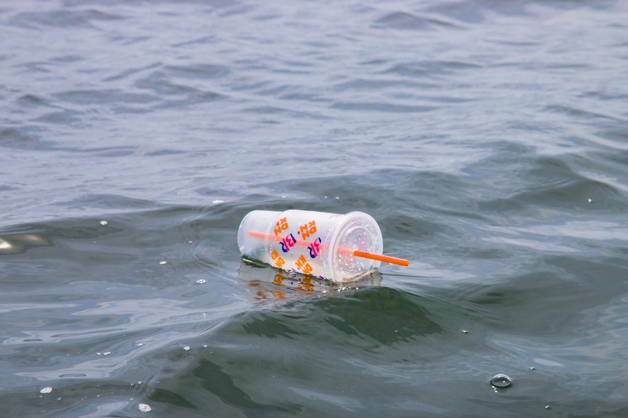 A single use plastic cup and straw float in the ocean