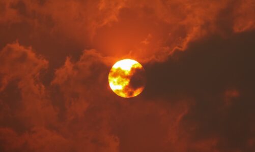 The sun set against an orange sky and partially hidden by wildfire smoke