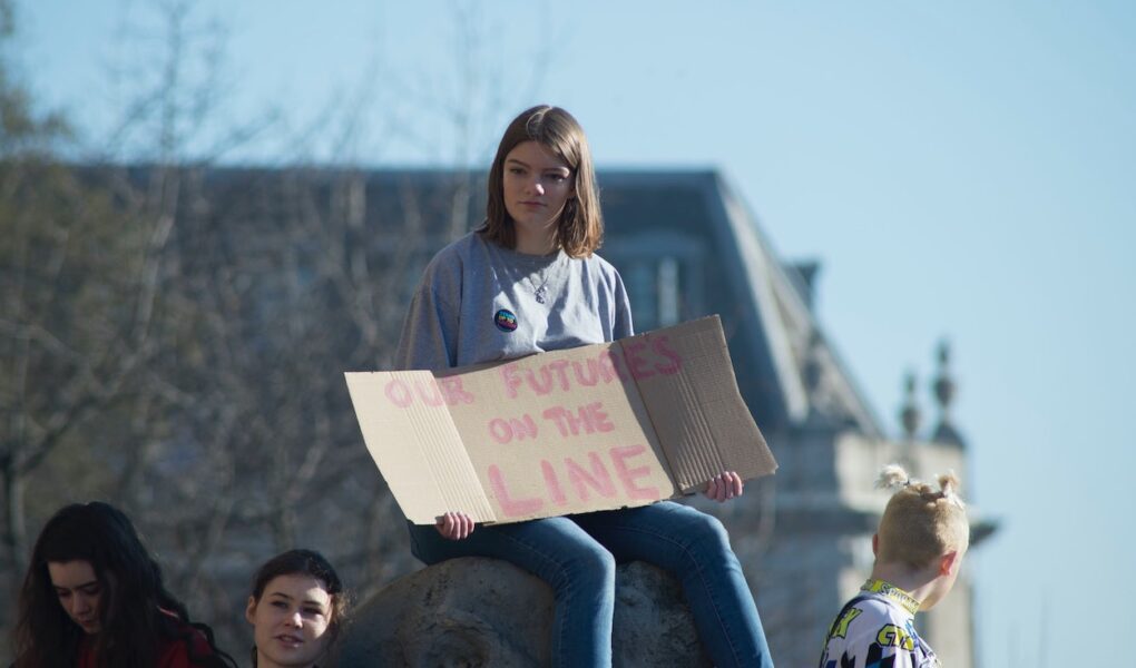 A teenage girl at an outdoor gathering holds a sign saying "Our Future is on the Line."