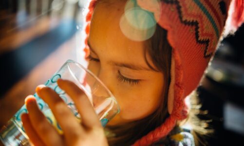 A young girl drinks water out of a glass on a sunny day