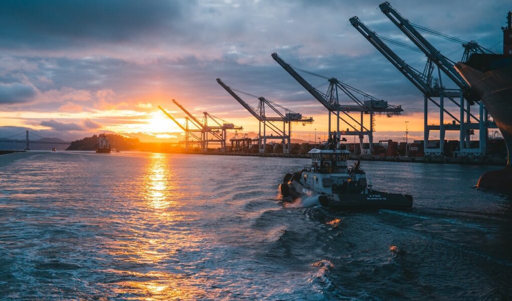Dock cranes stand silhouetted against a setting sun