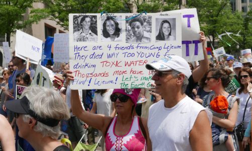 The 2017 People's Climate March in Washington D.C. with a woman holding a banner showing four friends who died from drinking toxic water near camp Lejeune