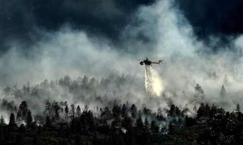 A firefighting helicopter drops fire retardant over a wildfire.
