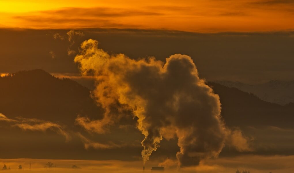 A birds-eye view of smokestack emissions from a power plant set against an orange sky.