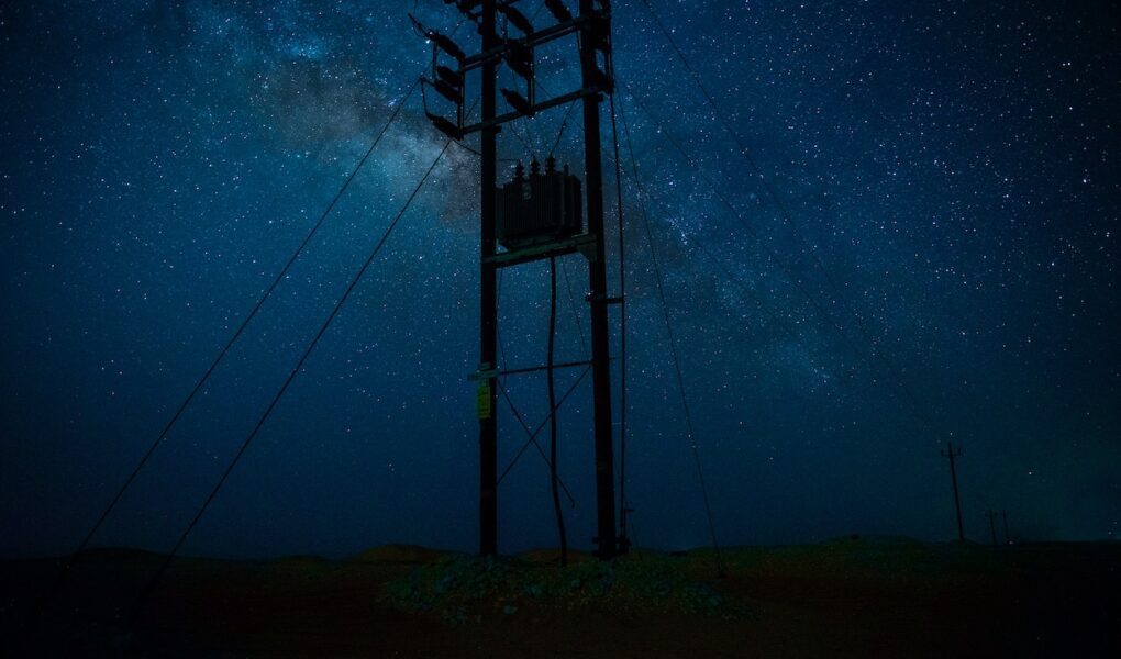 An electrical transmission tower silhouetted against a starry night