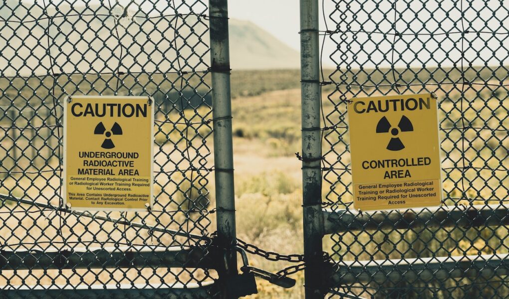 A chained fence gate with signs warming of radioactive waste beyond.